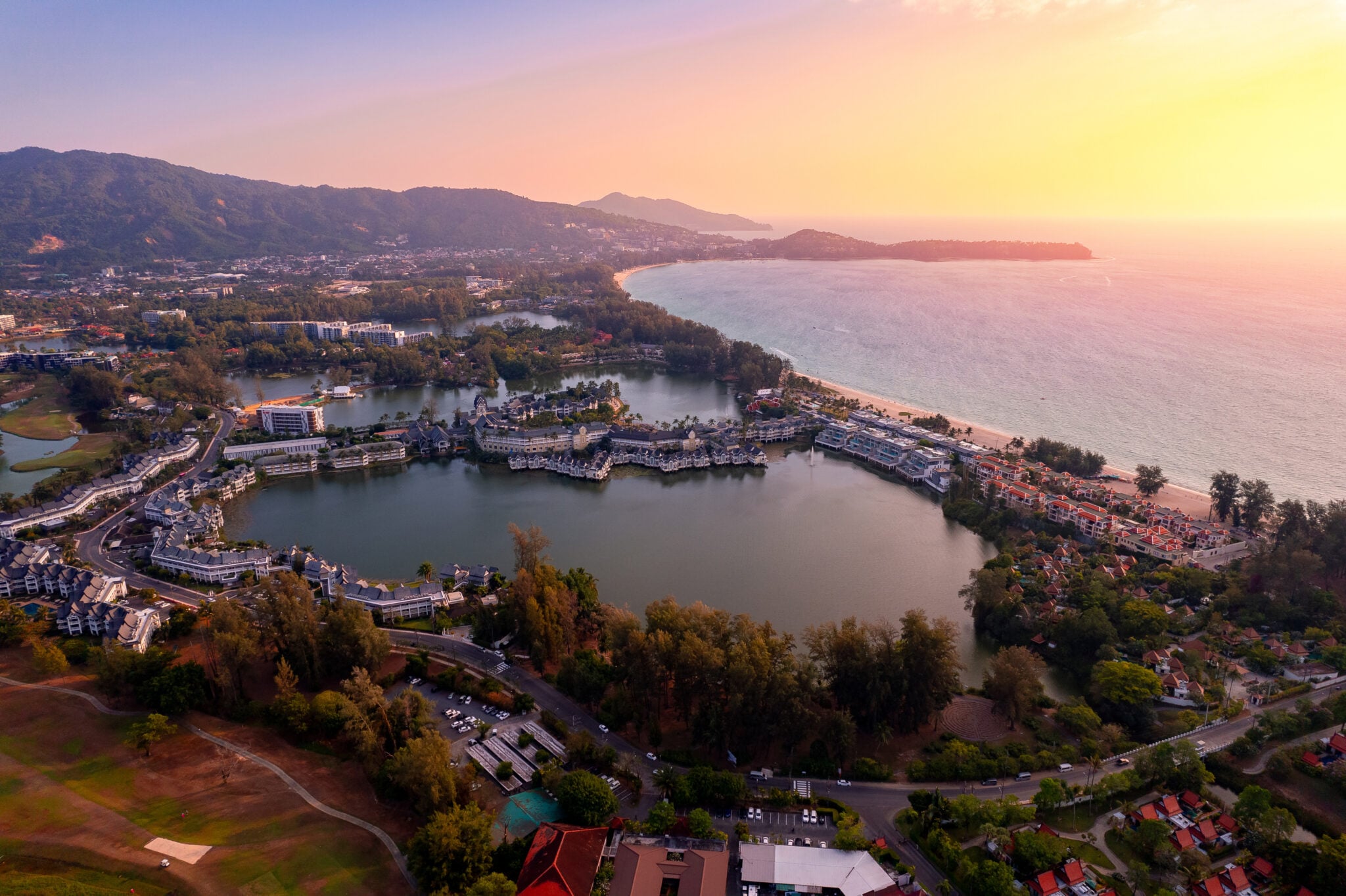 Aerial sunset view of Bang Tao lagoons and beach with luxury resort hotels and coastal development.