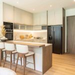 Modern luxury kitchen with white cabinetry, black appliances, wooden island with white bar stools, and underlit counter lighting