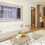Luxury bedroom with ensuite bathroom, flat-screen TV above white cabinetry, and walk-in wardrobe with warm lighting.
