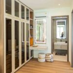 Luxury walk-in wardrobe with wooden cabinetry, glass doors, and ensuite bathroom access
