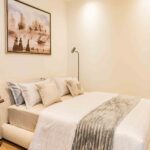 Modern bedroom with cream upholstered bed, neutral décor, framed artwork, and wooden flooring