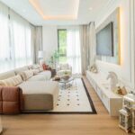 Modern luxury living room with cream L-shaped sofa, wall-mounted TV, wooden flooring and floor-to-ceiling windows