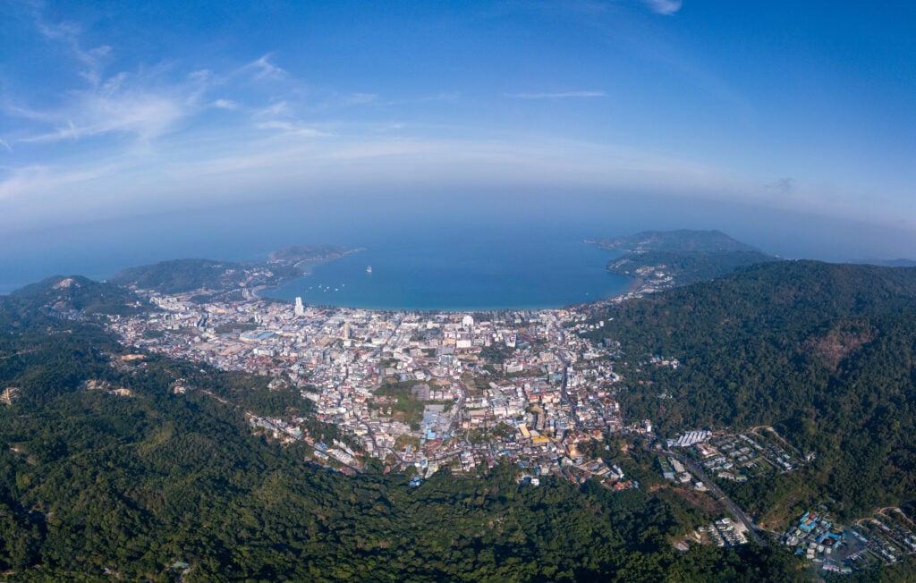 Aerial view of Patong beach and coastal town surrounded by forested hills and turquoise waters.